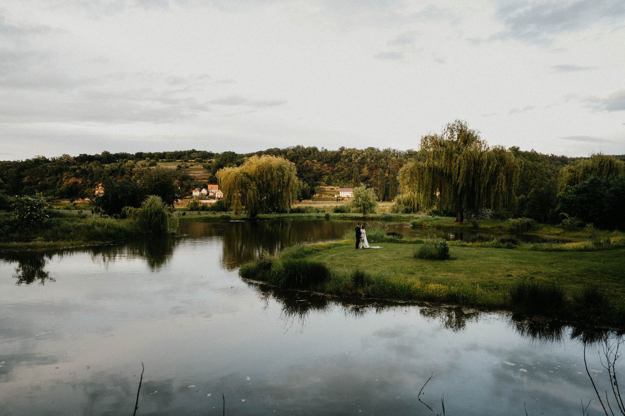 Ein Brautpaar am Ufer des großen Teichs, Weiden spiegeln sich im Wasser